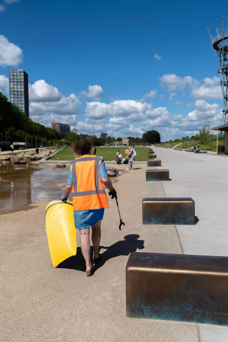 Met een afvalgrijper en de ene hand en een gele afvalzak in de andere op zoek naar zwerfafval Met een afvalgrijper en de ene hand en een gele afvalzak in de andere op zoek naar zwerfafval